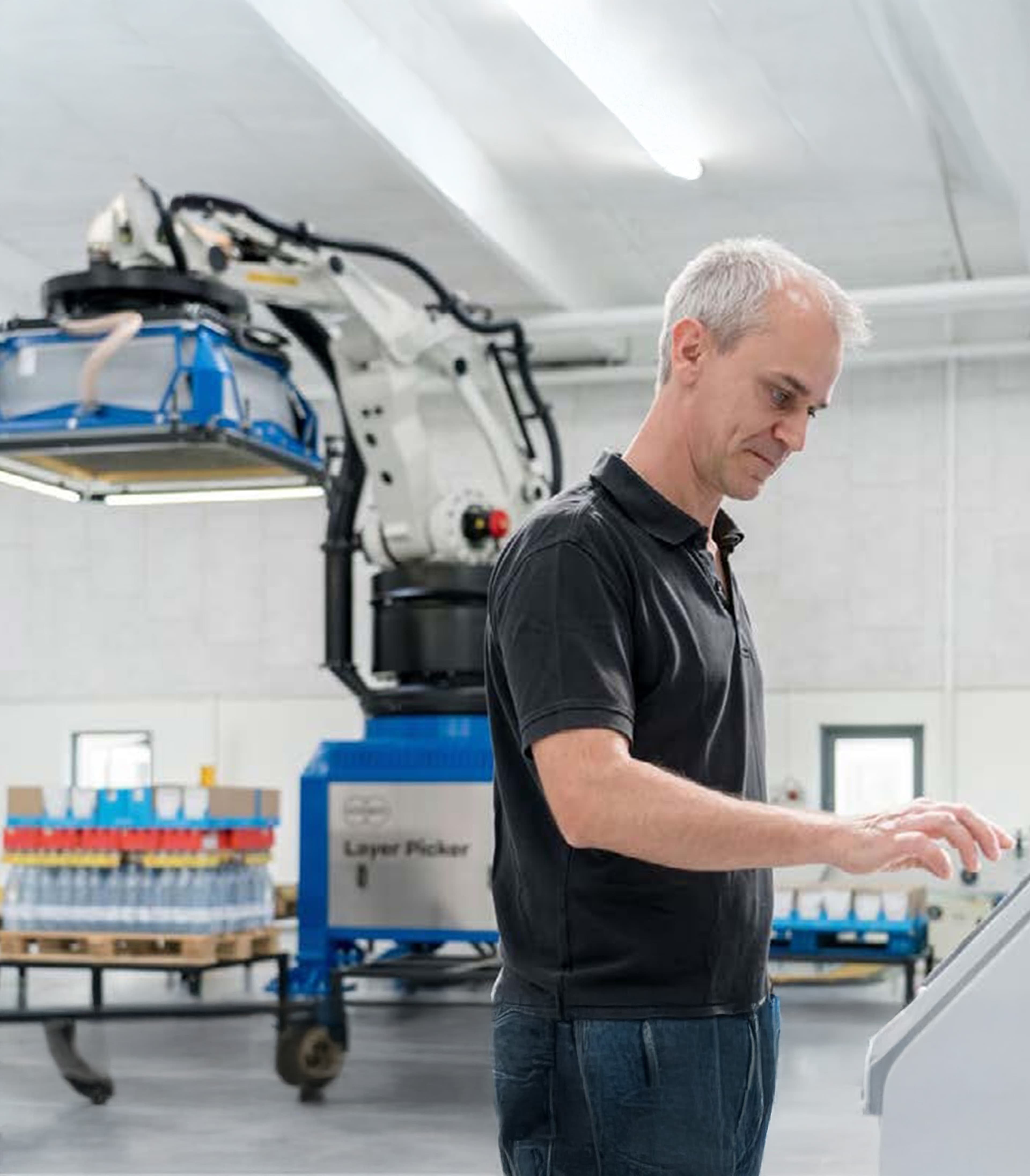 Engineer operating a control panel in front of an industrial robot arm that transports packaged goods.