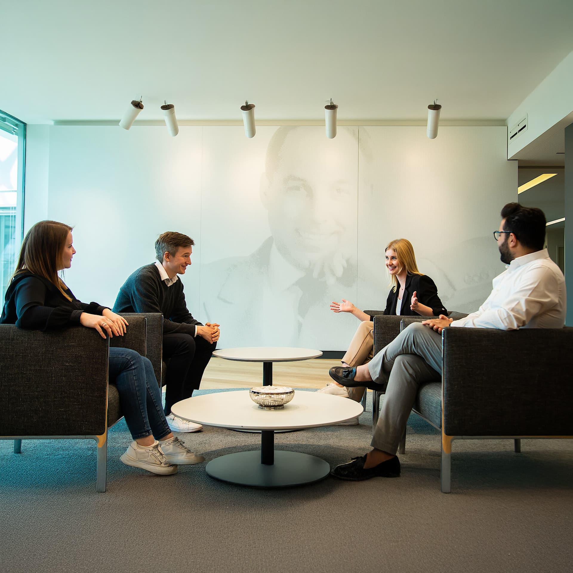 Group of people gathered around a table talking in an office setting.