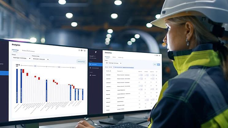 Eine Frau, die einen Schutzhelm und eine Sicherheitsweste trägt, konzentriert sich auf zwei Computerbildschirme.