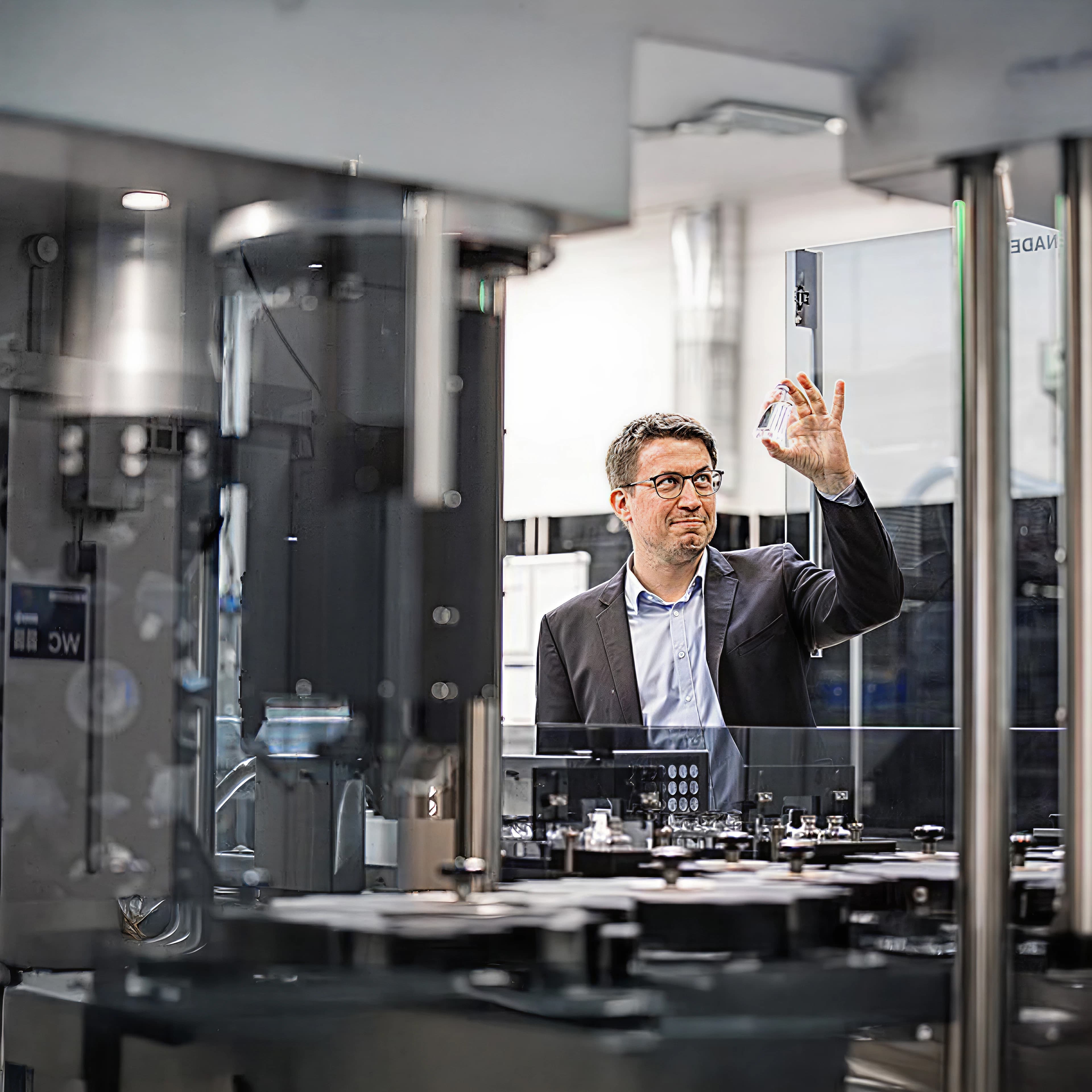 Mann hält eine kleine Glasflasche in einer Verarbeitungsanlage hoch.