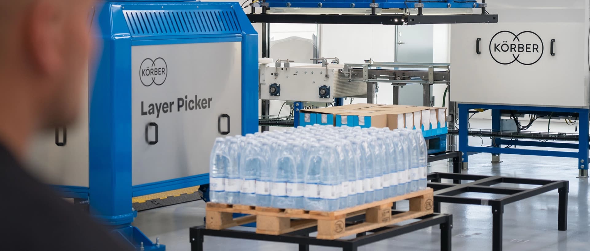 A man stands by Körber's layer picker technology, which is actively producing bottles.