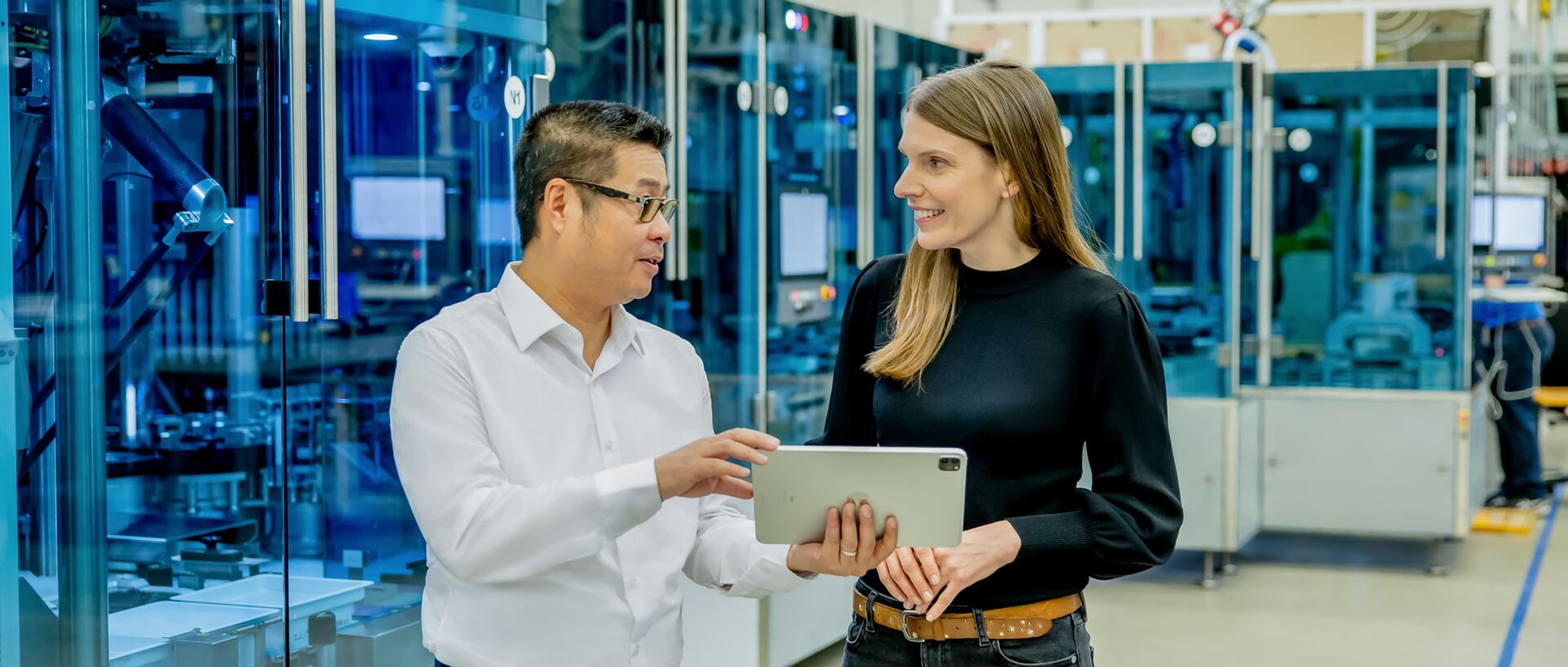 A man holding a tablet device and talking to a women in a factory environment
