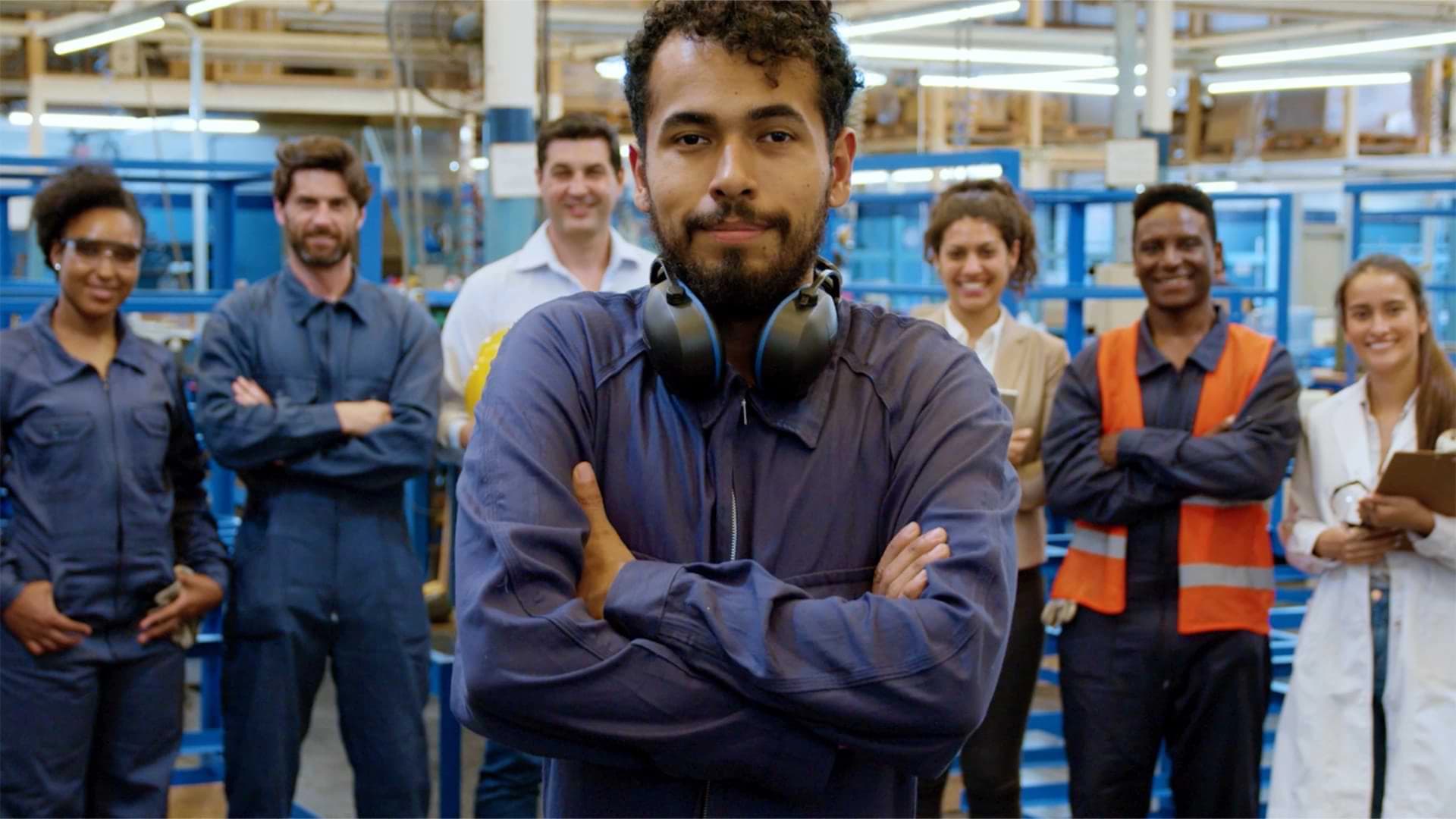 A group of diverse individuals standing together inside a factory, surrounded by machinery and industrial equipment.