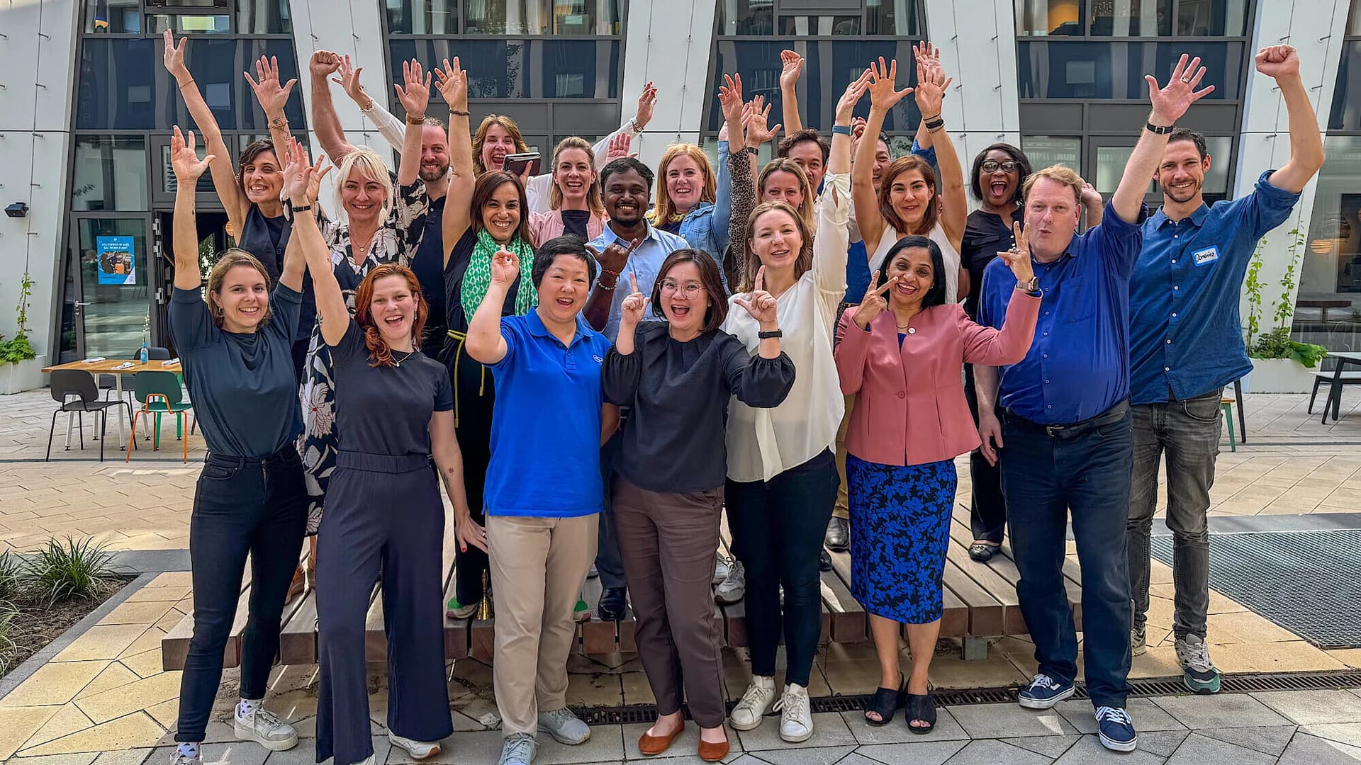 Eine Gruppe verschiedener Personen, die lächelnd vor einem großen Gebäude posieren.