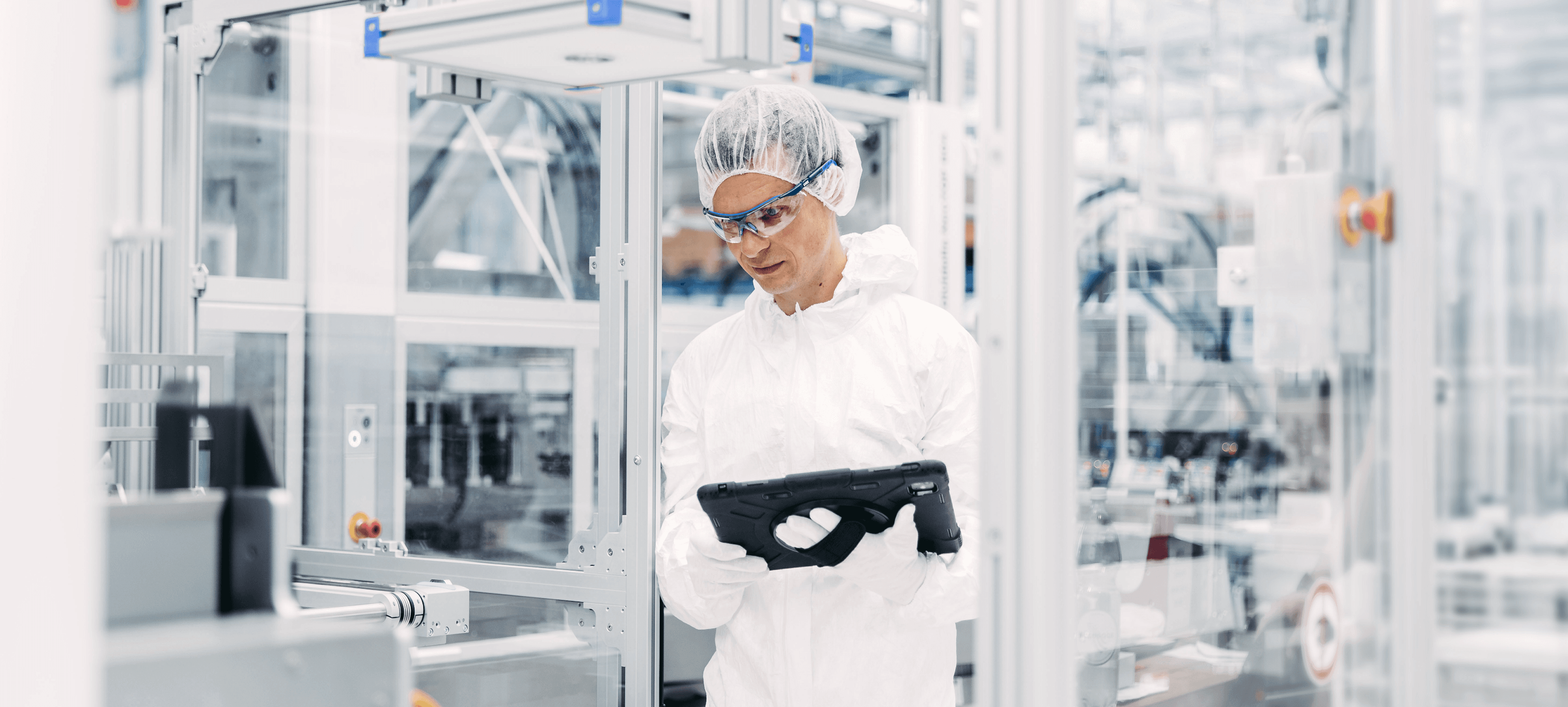 Technician wearing personal protective equipment holding a tablet device in a sterile environment