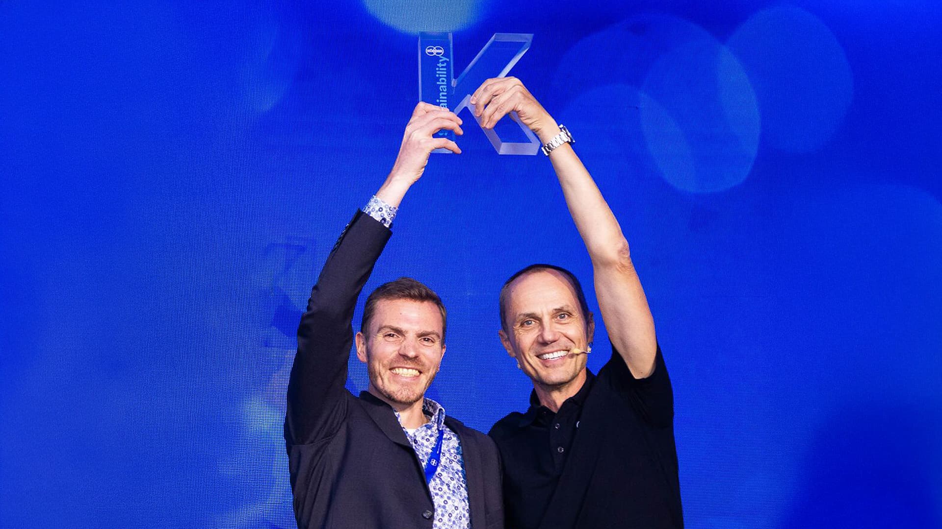 Zwei männliche Körber-Mitarbeiter halten ein Glas in Form eines K über ihren Köpfen.