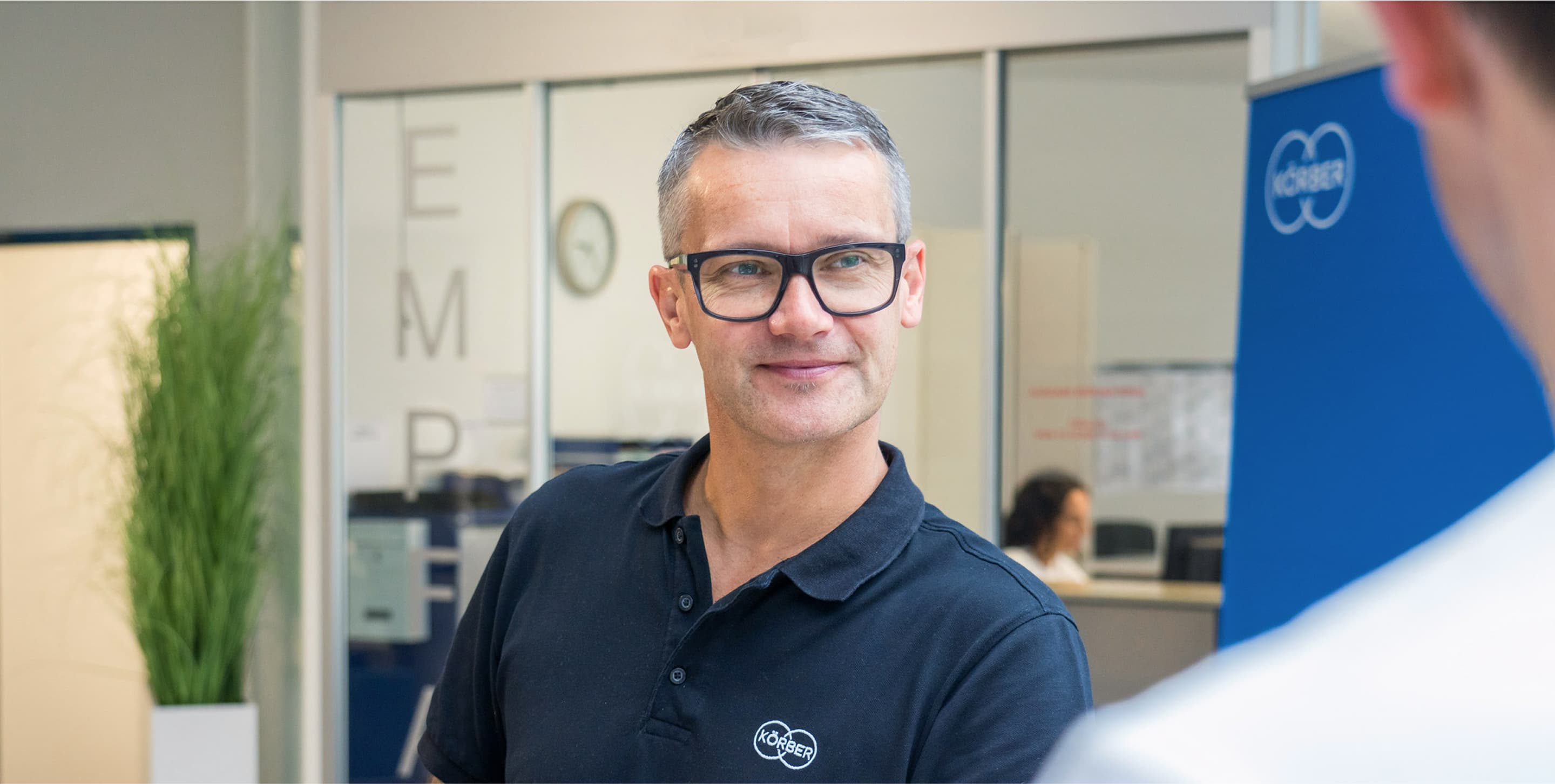 Mann mit schwarzer Brille und schwarzem Körber-T-Shirt lächelt