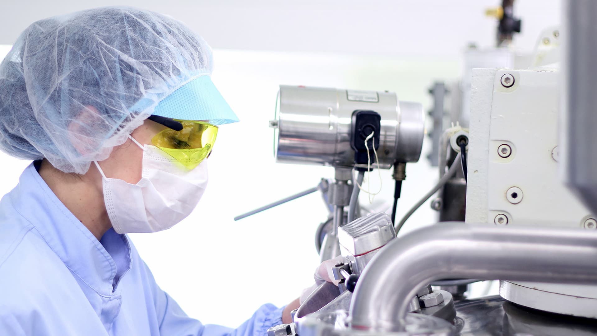 Person mit persönlicher Schutzausrüstung beim Blick in ein Mikroskop